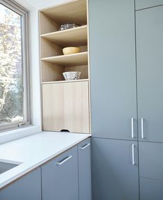 a kitchen with gray cabinets and white counter tops next to a large window that looks out onto the woods