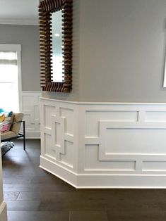 a living room with white walls and wood trimming on the wall, in front of a mirror