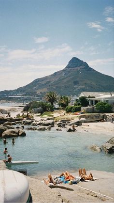 some people are laying on the beach and swimming in the water with a mountain in the background