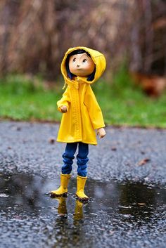 a toy doll wearing a yellow raincoat and blue jeans stands in the middle of a puddle