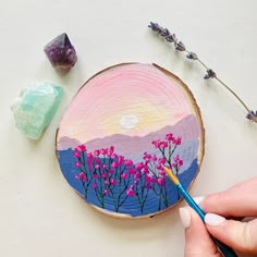 a person is holding a paintbrush in front of a painted wood slice