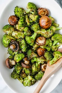 broccoli and mushrooms in a white bowl with a wooden spoon on the side