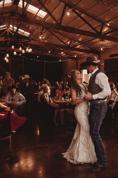 a bride and groom dance together in the middle of a room with people sitting at tables