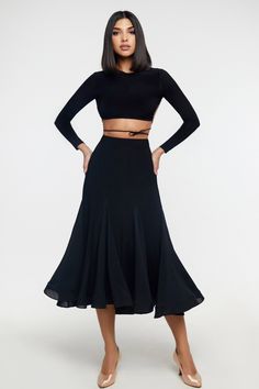 a woman wearing a black skirt and cropped top with her hands on her hips