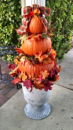 a tall white vase filled with lots of pumpkins and fall leaves sitting on top of a sidewalk