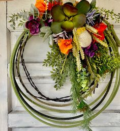 a wreath with flowers and greenery hanging on a door