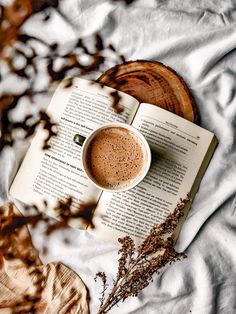 an open book with a cup of coffee on top of it next to some dried plants