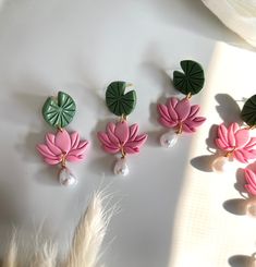 four pink and green flowers with pearls hanging from them on a white surface next to feathers