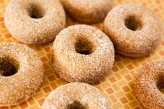 six sugared donuts sitting on top of an orange and yellow checkered table cloth