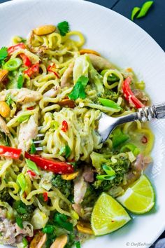 a white plate topped with pasta and vegetables next to a lime wedge on a table