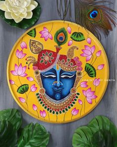 a yellow plate with a blue face painted on it next to some green leaves and flowers