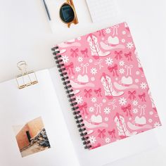 a pink notebook with white flowers and hearts on it next to an eyeglasses