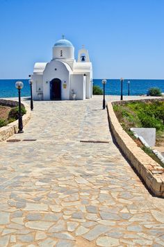 a white church on the coast with blue water in the background and cobblestone walkway leading up to it