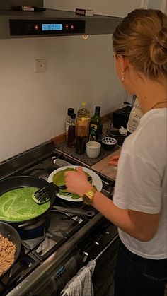 a woman cooking food on top of a stove next to a frying pan filled with green sauce