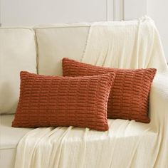 two orange pillows sitting on top of a white couch