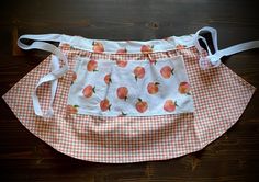 an orange and white checkered apron with apples printed on the front, attached to a wooden table