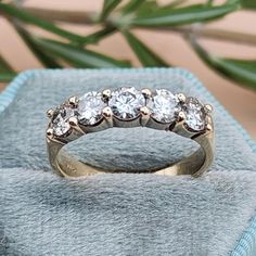 a diamond ring sitting on top of a blue velvet box next to a green plant