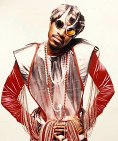 a man with sunglasses on his head and some beads around his neck, standing in front of a white background