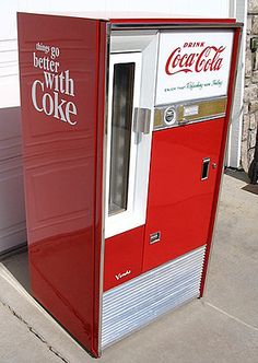 an old fashioned coca - cola machine sits on the sidewalk in front of a garage