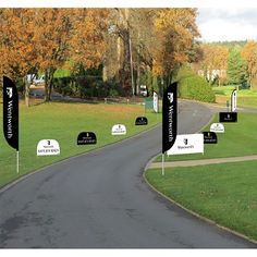 several black and white golf flags on the side of a road with trees in the background