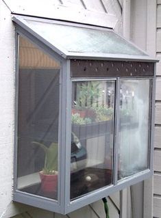 a window on the side of a house with potted plants in it's windowsill