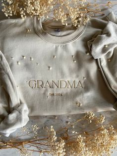 a white sweater with the word grandma on it next to some dried flowers and plants