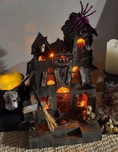 a halloween house made out of wood with lights and decorations around it on a table