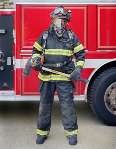 a fireman standing in front of a fire truck holding a stick and wearing a helmet