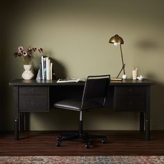 a desk with a lamp, books and flowers on it in front of a green wall