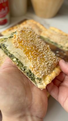 a person holding up a piece of food with sesame seeds on it and other items in the background