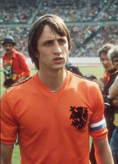 a man in an orange shirt standing on a soccer field with other people behind him