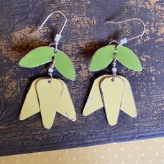 two pairs of green and yellow earrings with leaves hanging from the hooks on a piece of wood