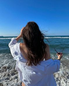 a woman standing on top of a beach next to the ocean holding a pair of scissors