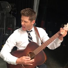 a man in a white shirt and tie is playing an acoustic guitar with his mouth open