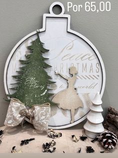 an ornament with a ballerina and christmas tree on it next to pine cones