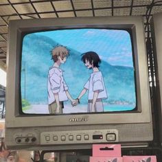 an old tv sitting on top of a shelf in front of a sign with anime characters