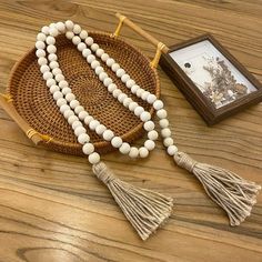 a wooden beaded necklace with tassels sits on a basket next to a framed photograph