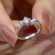 a woman's hand holding an engagement ring with three diamonds on top of it