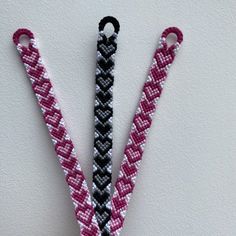 two pink and black lanyards hanging from a hook on a white wall next to a pair of scissors