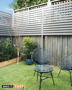 two chairs sitting on top of a lush green field next to a wooden privacy fence