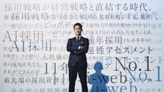 a man in a suit and tie standing with his arms crossed next to a wall that has words all over it