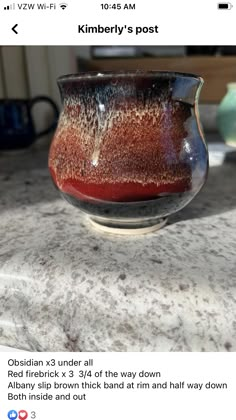 a red and black bowl sitting on top of a counter next to a cup filled with liquid