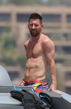 a shirtless man standing next to a surfboard on the roof of a car