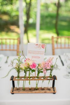 flowers in vases on a wooden stand at a table with white linen and greenery