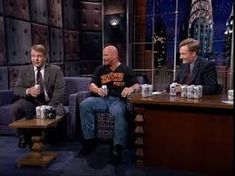 three men sitting on couches in front of a tv screen talking to each other