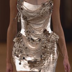 a woman in a white dress with lots of beads on her chest and arms, walking down a runway