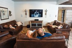 two people laying on couches in a living room with a flat screen tv above them