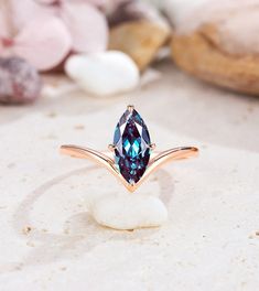 an image of a ring with a blue stone in it on a white rock next to flowers