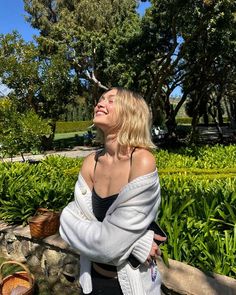 a woman is standing in front of some plants and looking up at the sky with her eyes closed