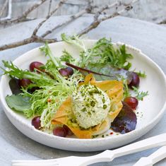 a white plate topped with salad and fruit on top of a table next to utensils